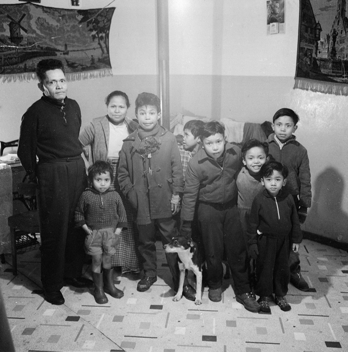 Vader, moeder en hun zeven kinderen in het kamp. Aan de muur links een wandkleed met een Hollands landschap.